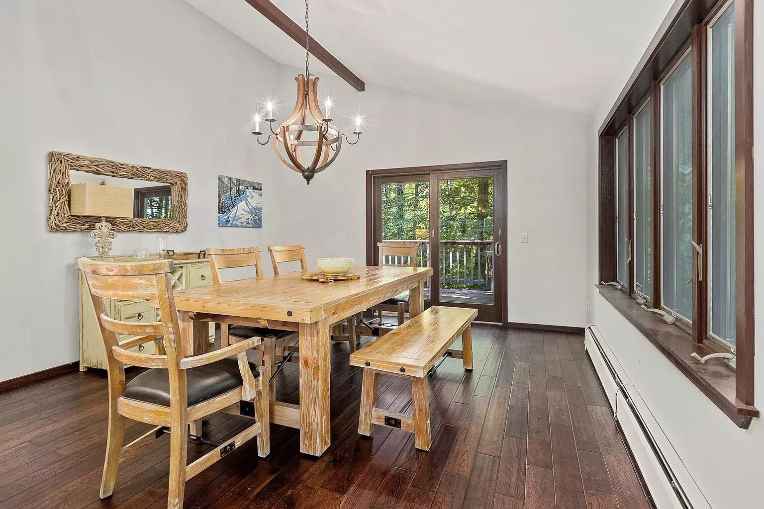 A dining area with a wooden table and chairs, a chandelier, and a view through a glass door.