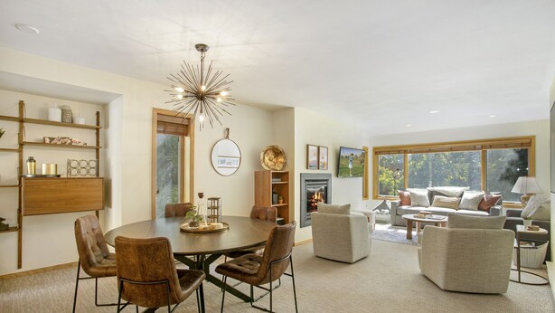 A modern living room with a round dining table, leather chairs, a fireplace, and a large window offering a view of the outdoors. - Modern Vail Retreat, Free Shuttle, Fireplace & Mountain Views | SF201 (Vail)