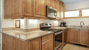 A kitchen with wooden cabinets, granite countertops, stainless steel appliances, and a window providing natural light. - Modern Vail Retreat, Free Shuttle, Fireplace & Mountain Views | SF201 (Vail)