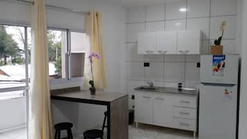 Una cocina moderna con armarios blancos, un lavamanos empotrado y un refrigerador. Se aprecia una pequeña isla con taburetes y una planta en maceta.