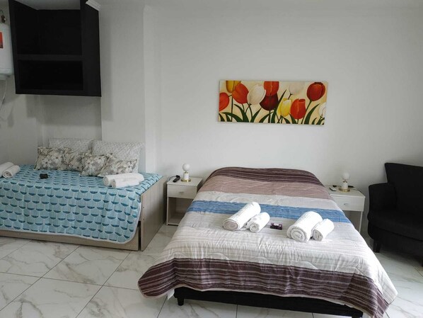 A hotel room with two beds, a painting of tulips, a black chair, and a TV mounted on the wall.