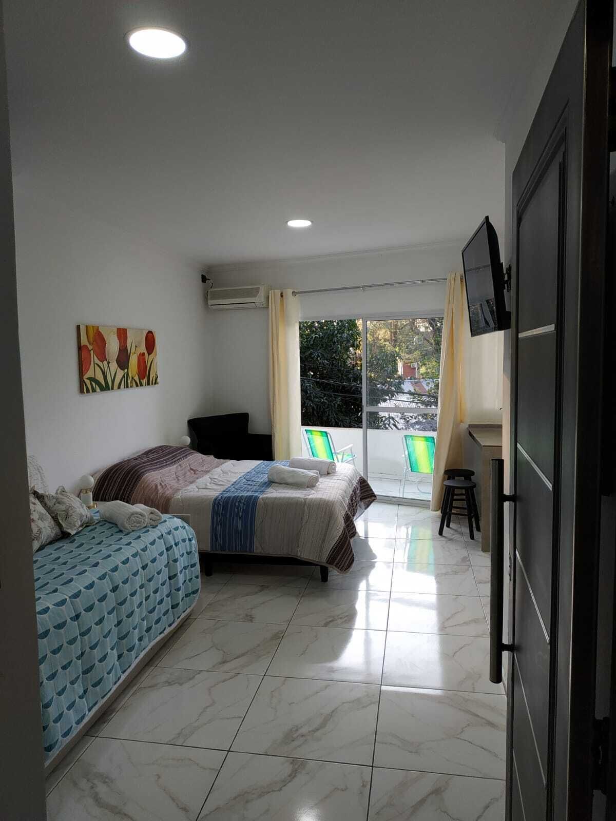 Un dormitorio con dos camas, un televisor y un balcón con sillas.
