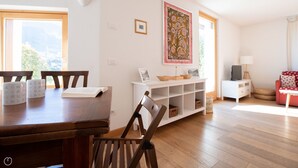 A dining area with a wooden table and chairs, a white console table with decorative items, and a red sofa in a bright room with wooden flooring and large windows. - Milano 35 - Three Bedroom Apartment, Sleeps 6 (Bormio)