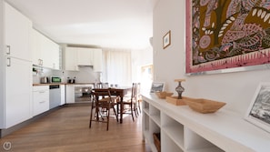 A modern kitchen with white cabinets, a wooden dining table, and a view of the dining area.