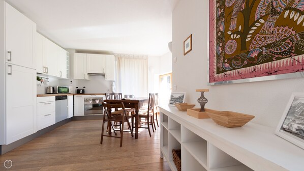 A modern kitchen with white cabinets, a wooden dining table, and a large window.