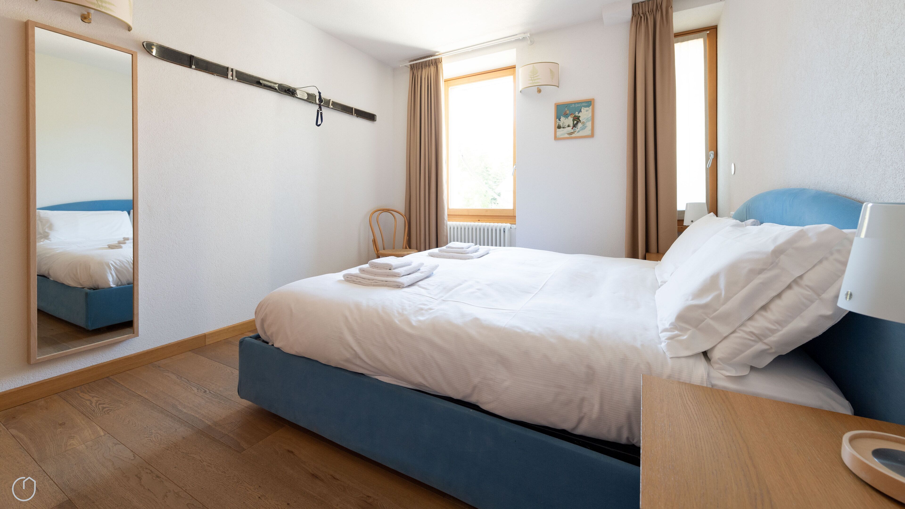 A hotel room with a bed, a chair, a window, and a mirror.