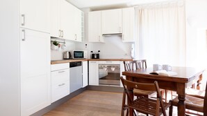 A modern kitchen with white cabinets, a built-in oven, and a dining area with wooden chairs and a table. - Milano 35 - Three Bedroom Apartment, Sleeps 6 (Bormio)