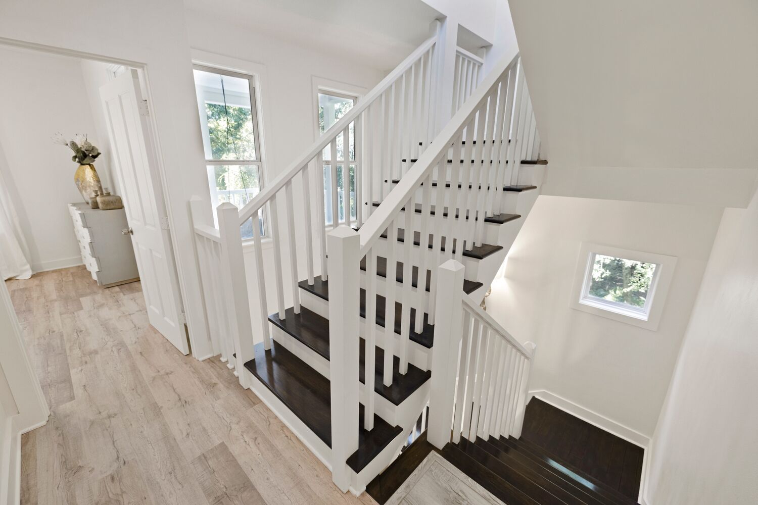 A staircase with white railings and dark steps, leading to a landing with a small window.
