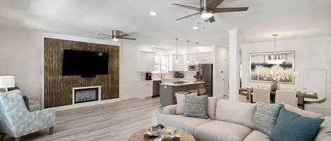 A modern living room with a fireplace, a dining area, and a kitchen.