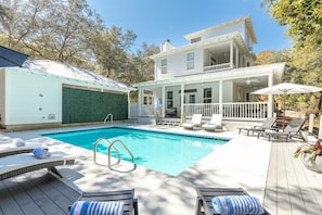 A swimming pool with lounge chairs and a deck, surrounded by a house with a balcony and a covered patio.