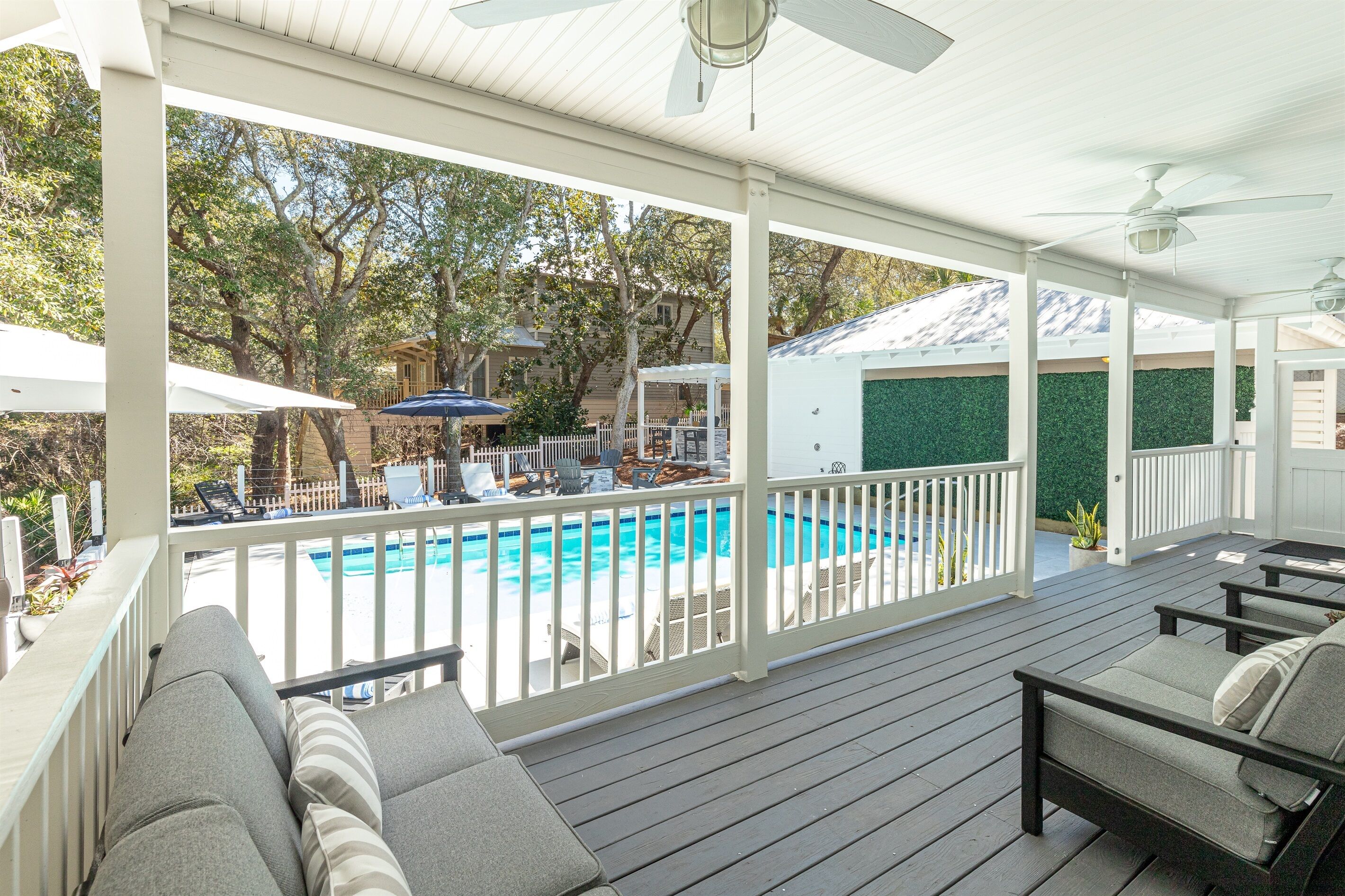 A covered deck with a pool, outdoor furniture, and a view of a house with a green wall.