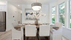 Une cuisine moderne avec une table à manger, des chaises, un lustre et une grande fenêtre.