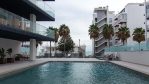Una piscina interior con sillones de descanso, palmeras y edificios modernos al fondo.