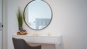 Un escritorio blanco con un espejo redondo, un florero con plantas verdes y objetos decorativos.