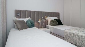 Una habitación de hotel con dos camas, un cabecero gris y una mesita de noche con lámpara.