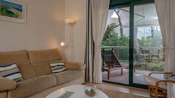 A living room with a beige sofa, a white coffee table, and a glass door leading to an outdoor area with a chair and a table. - Apartment in Pals with community pool (Pals)