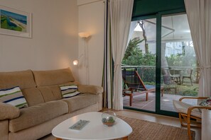 A living room with a beige sofa, a white coffee table, and a glass door leading to an outdoor area with a chair and a table. - Apartment in Pals with community pool (Pals)