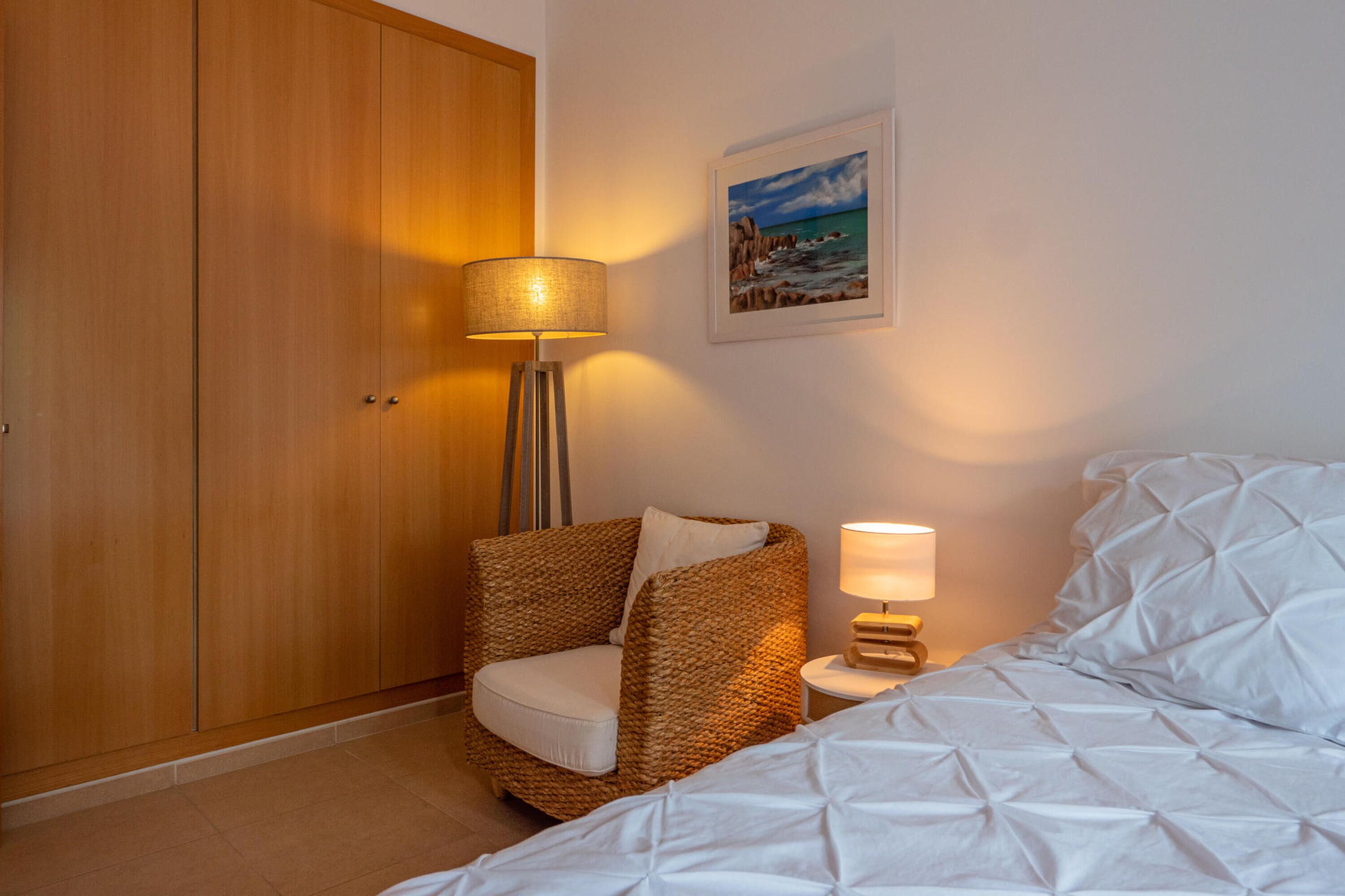 Une chambre à coucher avec un lit, une chaise, une lampe, une armoire et un tableau accroché au mur.