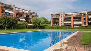 A rectangular swimming pool with a wooden deck and metal ladder, surrounded by modern apartment buildings with balconies and large windows. - Apartment in Pals with community pool (Pals)