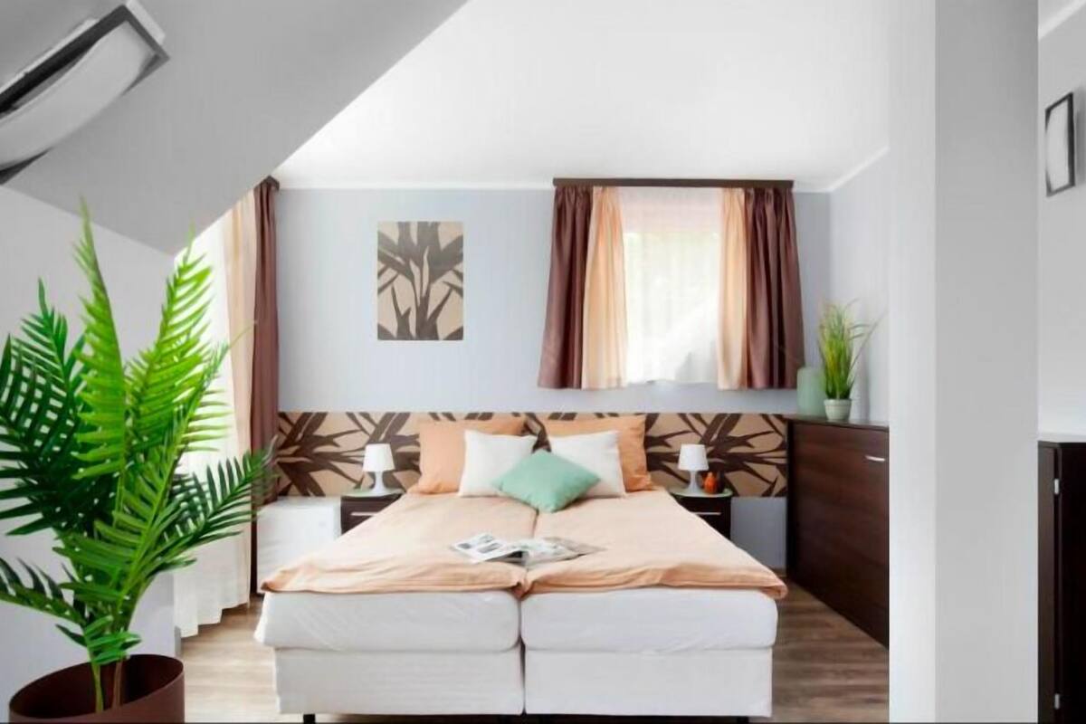 Un dormitorio moderno con cama, mesitas de noche, una planta y una ventana con cortinas.