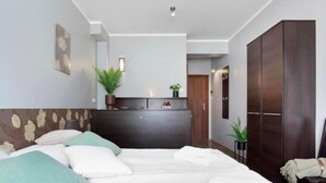 A modern bedroom with a large bed, a dark wooden wardrobe, a small desk, and a potted plant. - Guesthouse Baltic (Gdansk)