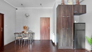 A modern kitchen with a dark wood cabinet, a stainless steel refrigerator, and a dining area with a table and chairs. - Guesthouse Baltic (Gdansk)
