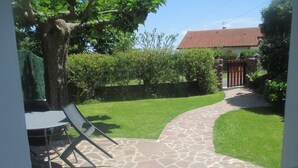 A stone patio leading to a house with a red-tiled roof, surrounded by a well-maintained lawn and a tree.