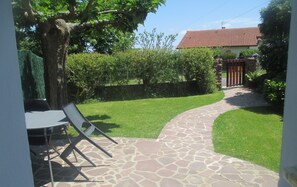 Un patio de piedra que lleva a una casa con techo de tejas rojas, rodeada por un césped cuidado y un árbol.