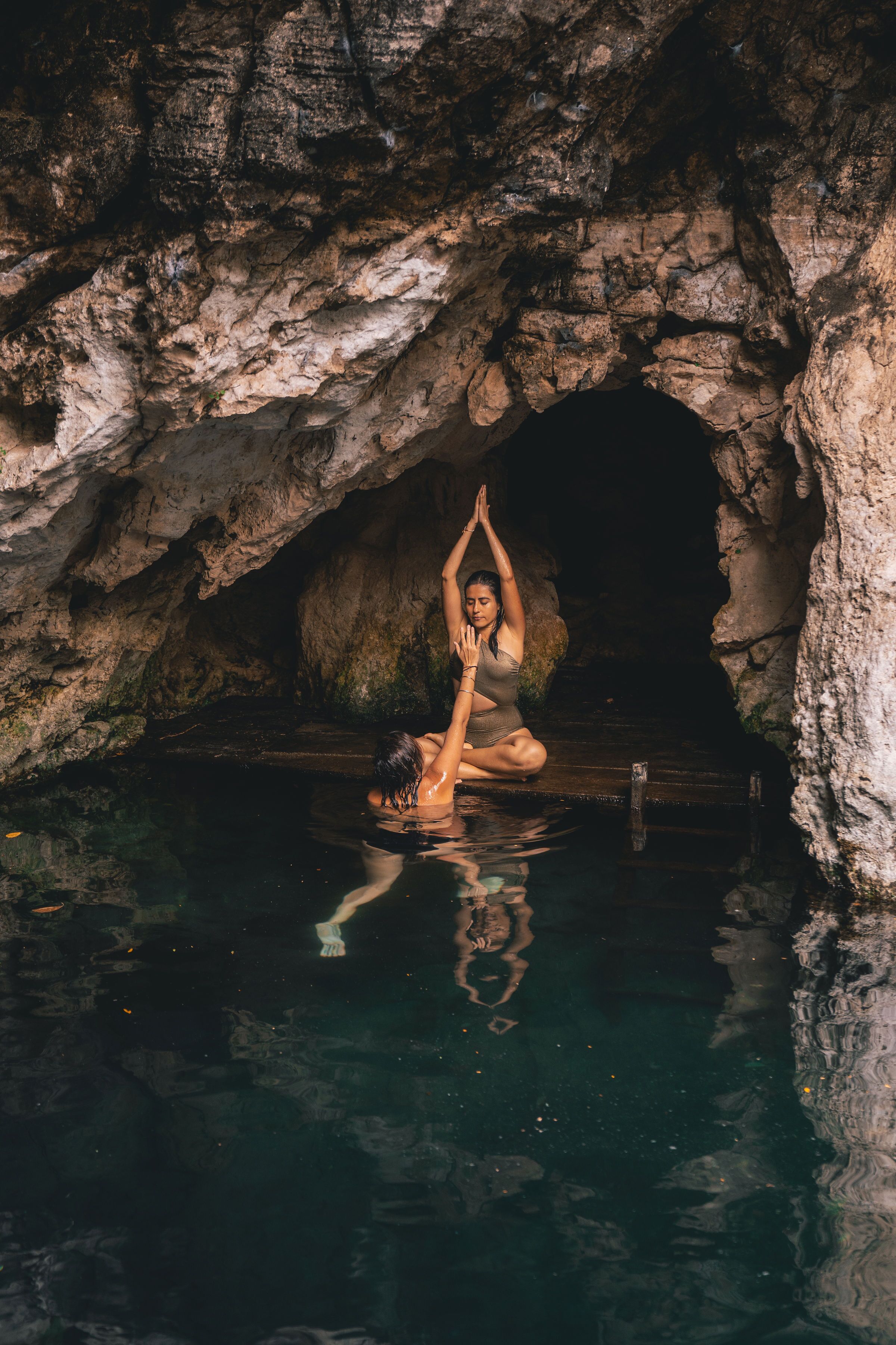 A person meditating in a cave with a pool.
