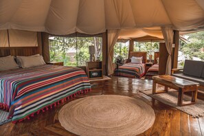 A tented accommodation with two beds, a sofa, and a round rug.