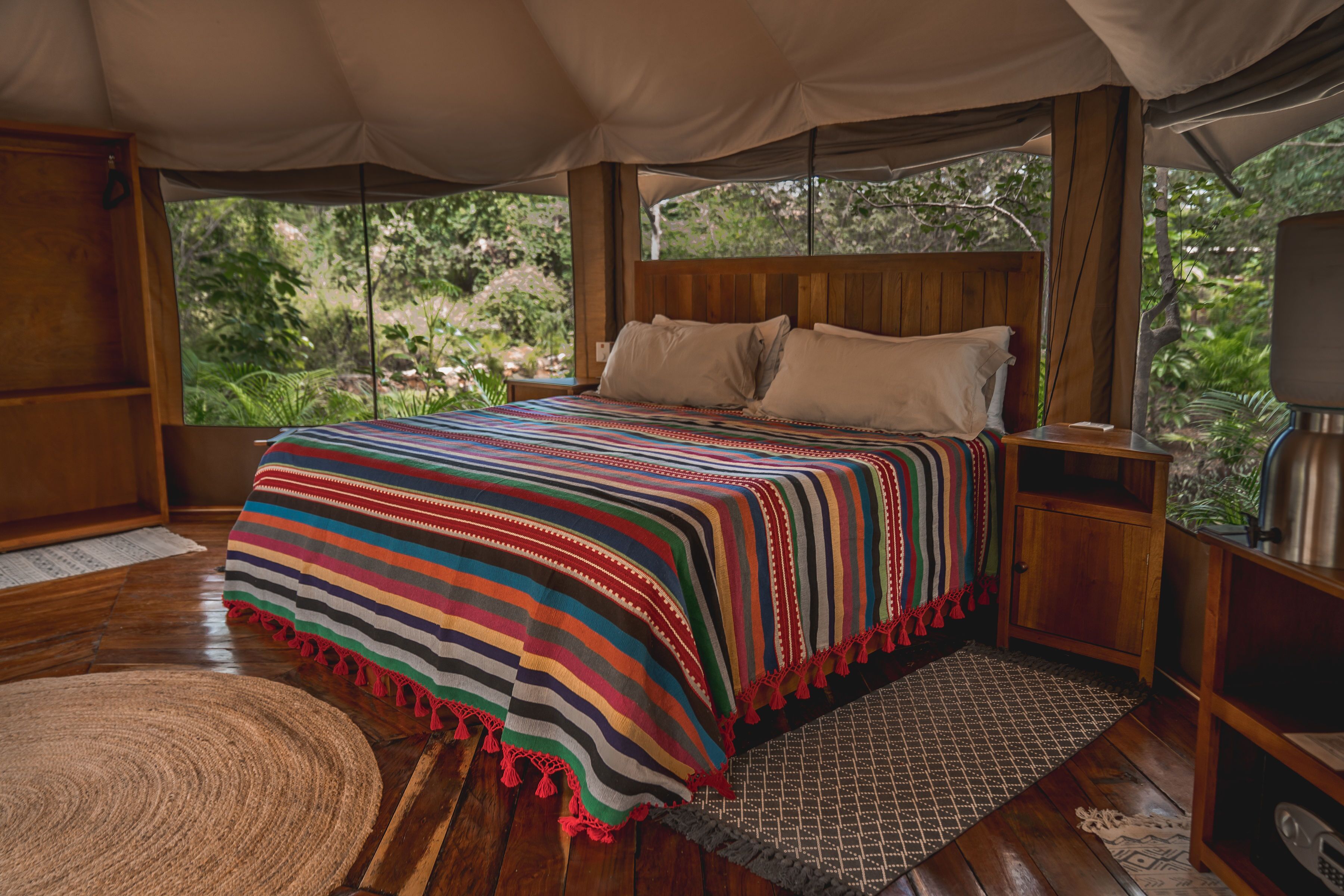 A spacious tented room with a large bed, wooden headboard, and a view of lush greenery outside.
