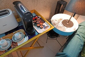 Een klein tafeltje met een koffiezetapparaat, een dienblad vol gebak en een bord met taart.