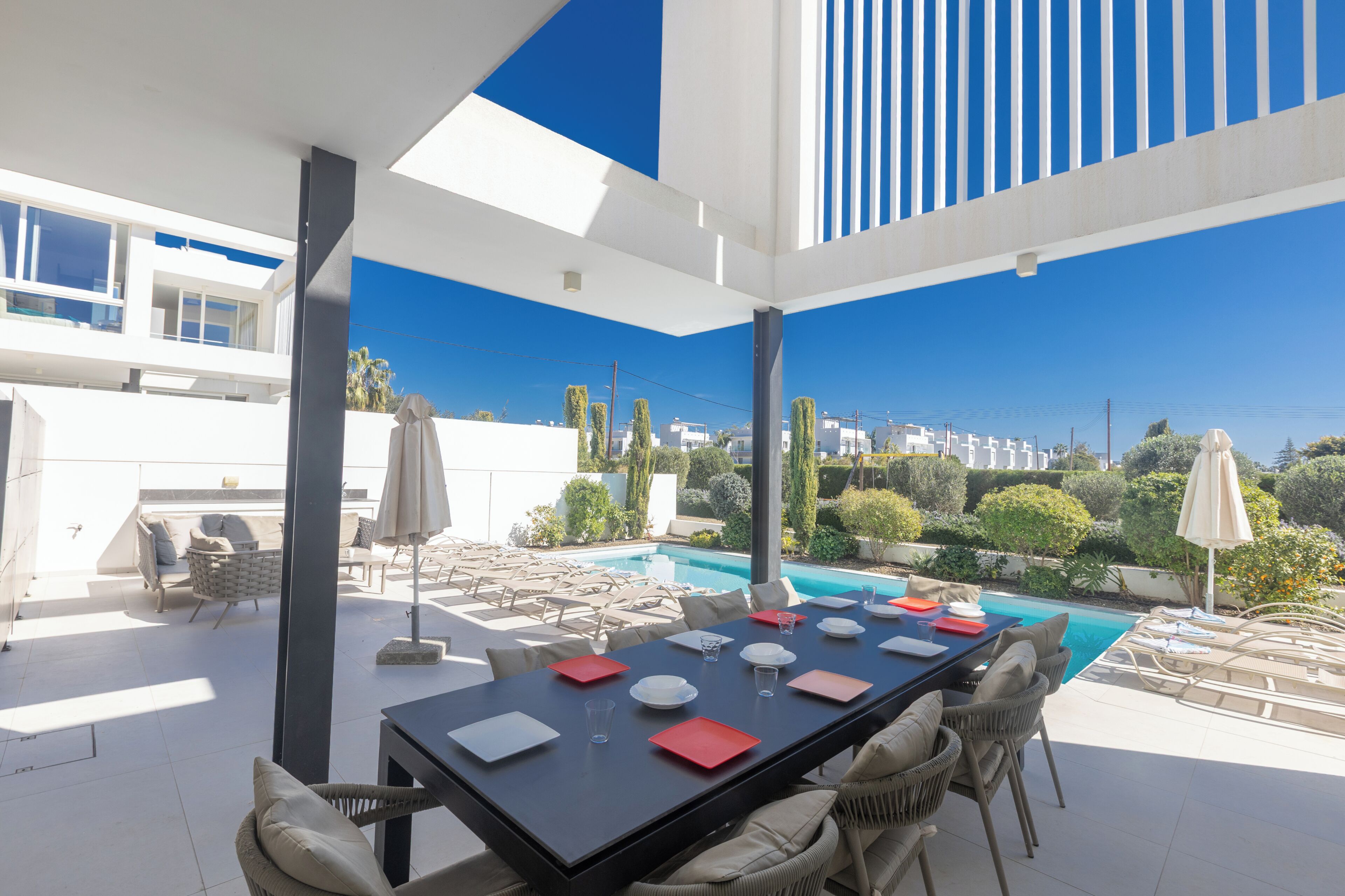 An outdoor dining area with a pool view, modern furniture, and a clear sky.