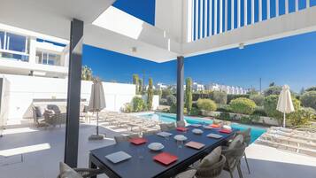 An outdoor dining area with a pool view, modern furniture, and a clear sky.