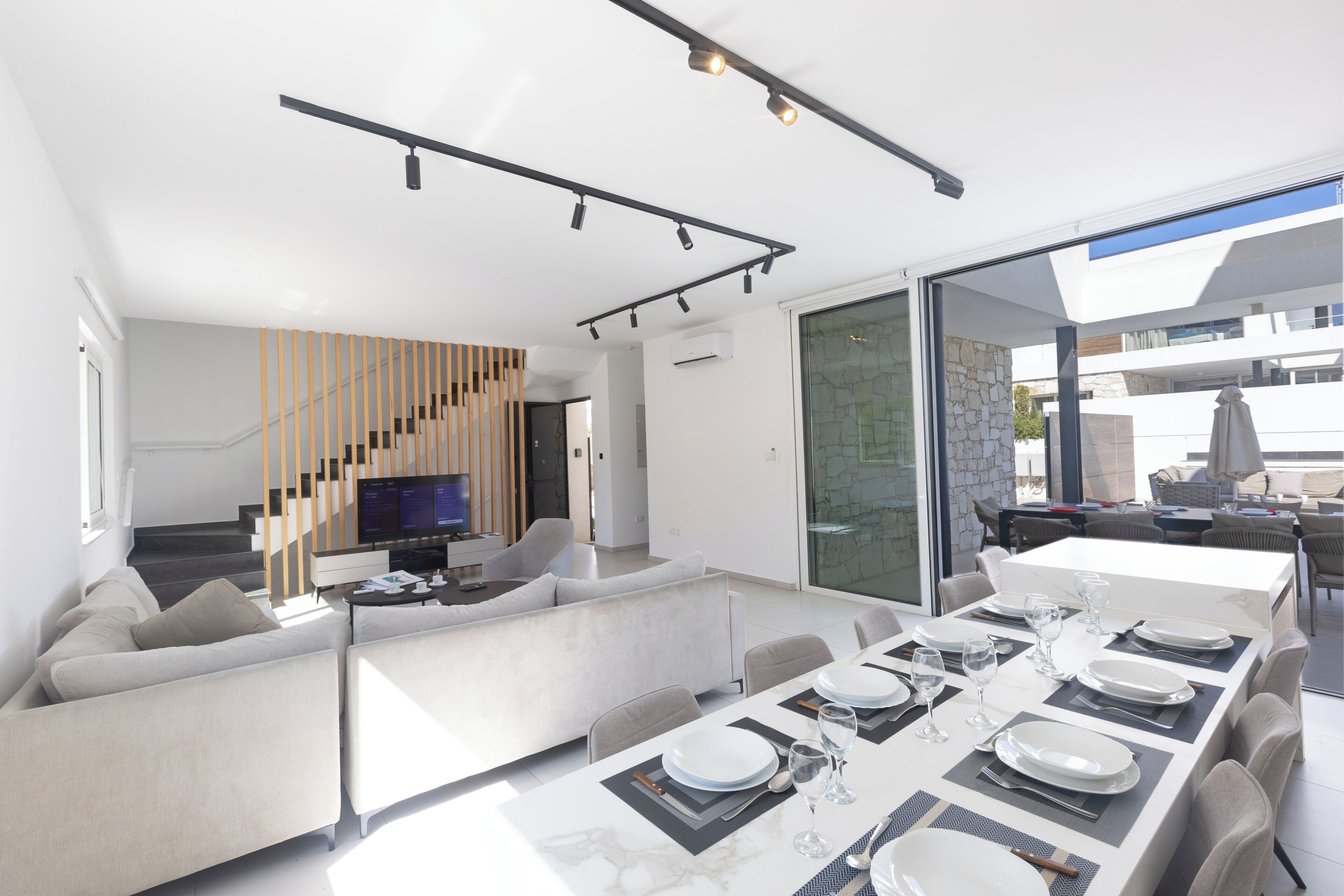 A modern interior with a dining area, sofa, TV, and staircase.