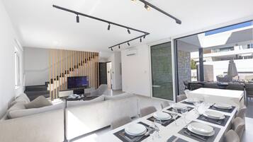 A modern interior with a dining area, sofa, TV, and staircase.