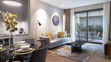 A modern living room with a sofa, coffee table, and dining area. There is a large window with a view of greenery outside.