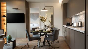 A modern kitchen with a dining area, featuring a flat-screen TV, pendant lights, and a marble backsplash.