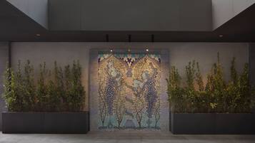 A building entrance with a mosaic wall and two planter boxes with greenery.