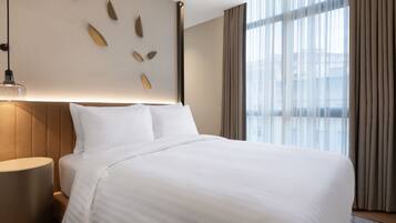 Une chambre d’hôtel avec un grand lit, une table de chevet, un luminaire fixé au mur et une fenêtre avec des rideaux.