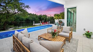 Eine moderne Terrassenanlage im Freien mit Pool, Holzmöbeln und Blick auf die umliegende Bepflanzung.