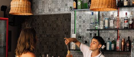 A bar area with wooden furniture, hanging wicker lamps, and shelves stocked with bottles.