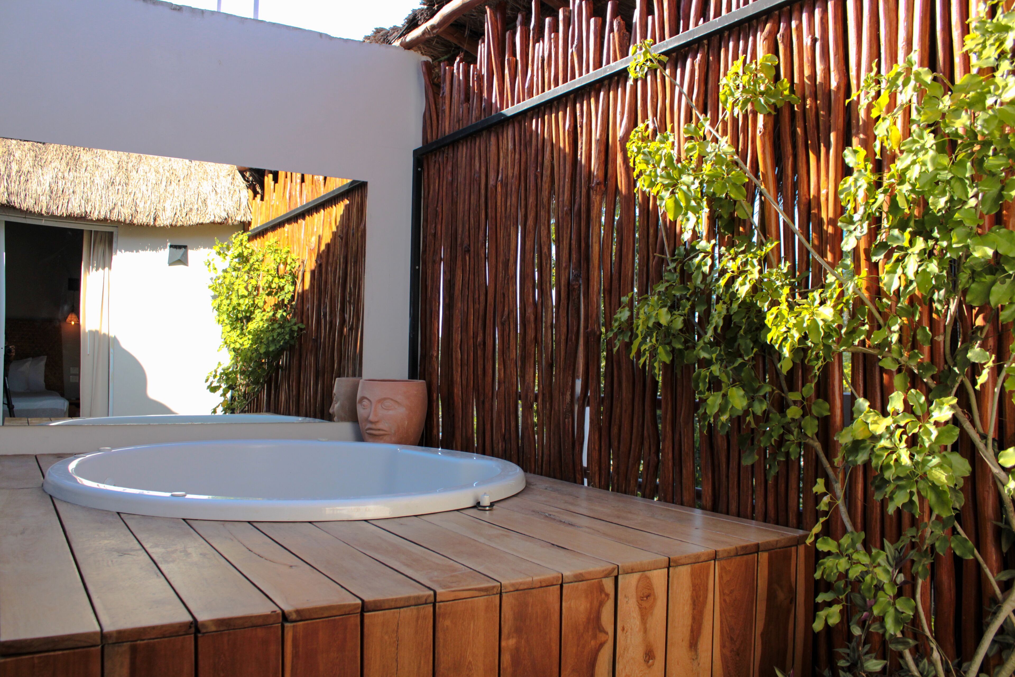 Una terraza de madera con un jacuzzi, una estructura de techo de paja y una valla de bambú.