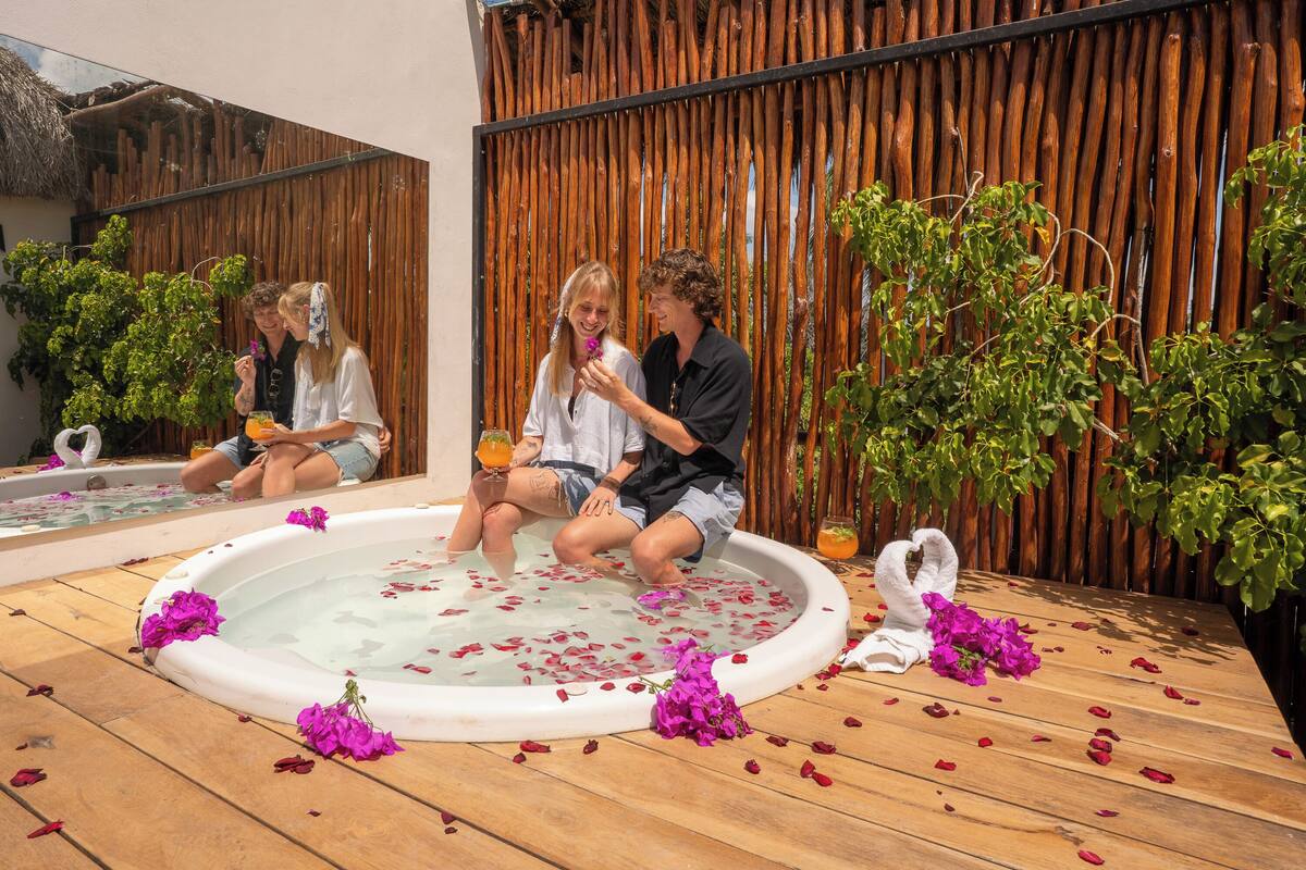 Un jacuzzi rodeado de cubierta de madera y paredes de bambú, con pétalos de rosa esparcidos.