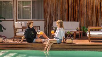 A poolside area with wooden deck, lounge chairs, and a bamboo wall.
