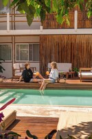 A poolside area with wooden deck, lounge chairs, and a bamboo wall.