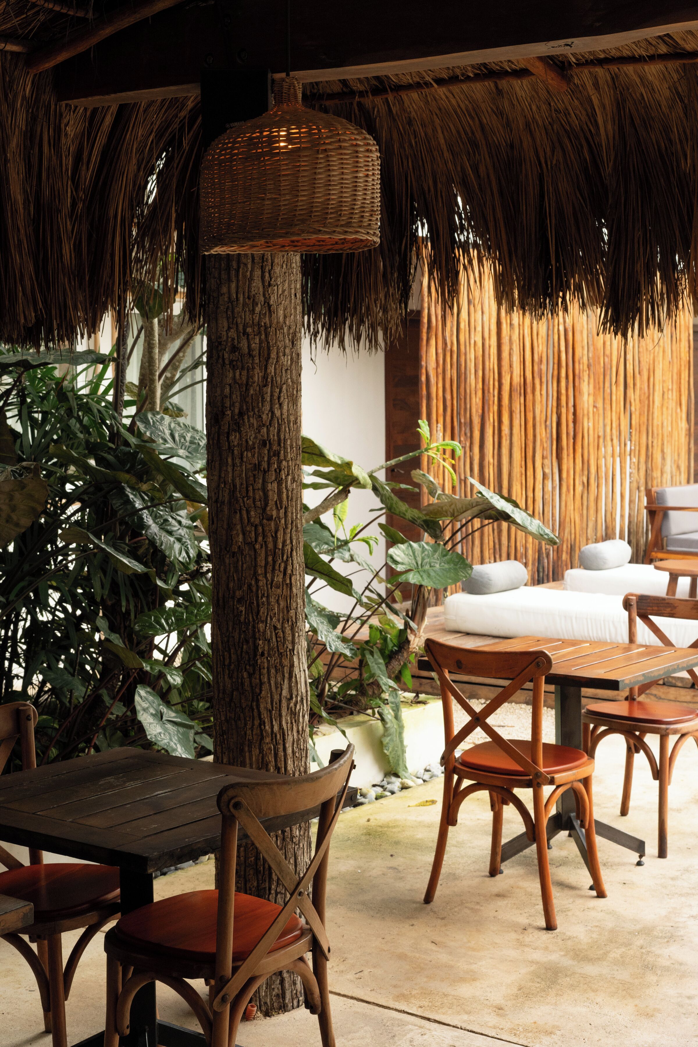 A wooden table with chairs, a wicker hanging light fixture, and a thatched roof structure.