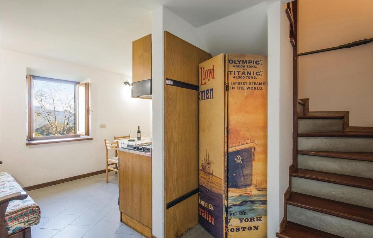 Una stanza con un armadio in legno, un tavolino, una sedia e una finestra vista alberi.