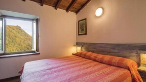 A bedroom with a bed, a window with a view of a mountain, a wall-mounted light, and a framed picture. - Studio apartment on 2 floors "Balzone 1" (Toscana)