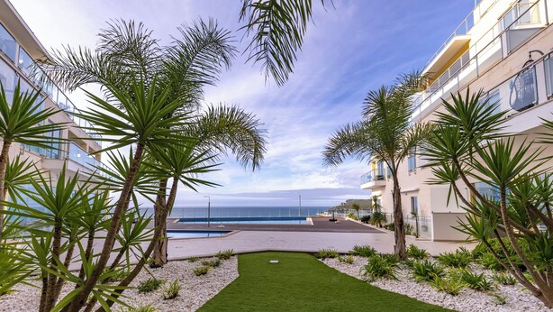 Ein angelegter Innenhof mit Palmen, einem Pool und Blick aufs Meer.
